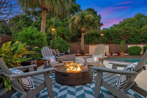 Un espacio al aire libre con sillas Adirondack, una chimenea y una piscina.