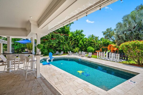 A swimming pool with a sunshade, lounge chairs, and a garden with various plants.
