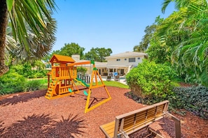A playground with a swing set and slide, surrounded by landscaped gardens and a building in the background. - Pool - Soccer - Basketball - Game Room - Sleeps 20 (Largo)