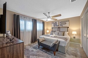 Une chambre d’hôtel équipée d’un lit, d’un bureau, d’une chaise, d’un ventilateur de plafond et d’une fenêtre avec des rideaux.