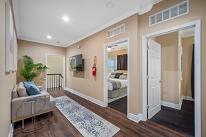 A hallway with a sofa, a glass coffee table, a patterned rug, a television, and a door leading to a bedroom.