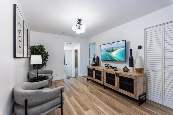 Una sala de estar moderna con un televisor de pantalla plana, un sofá gris, un mueble de madera y una planta.