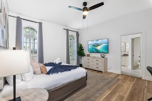 Un dormitorio moderno con cama, televisor, ventilador de techo y vistas al exterior.