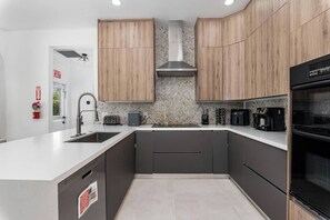 A modern kitchen with a central island, stainless steel appliances, and wooden cabinetry. - Family estate w/private pool & basketball court