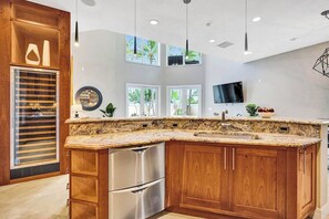 A kitchen with a granite countertop, stainless steel appliances, wooden cabinets, and a large window providing natural light. - Luxury villa w/pool, rooftop bar & fire pit (Pompano Beach)