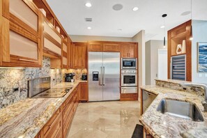 A modern kitchen with wooden cabinets, stainless steel appliances, and granite countertops. - Luxury villa w/pool, rooftop bar & fire pit (Pompano Beach)