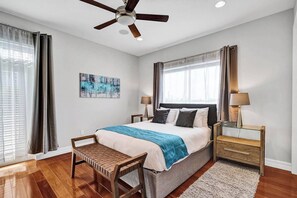 A bedroom with a bed, two bedside tables, a chair, a ceiling fan, and a window with curtains. - Luxury villa w/pool, rooftop bar & fire pit (Pompano Beach)