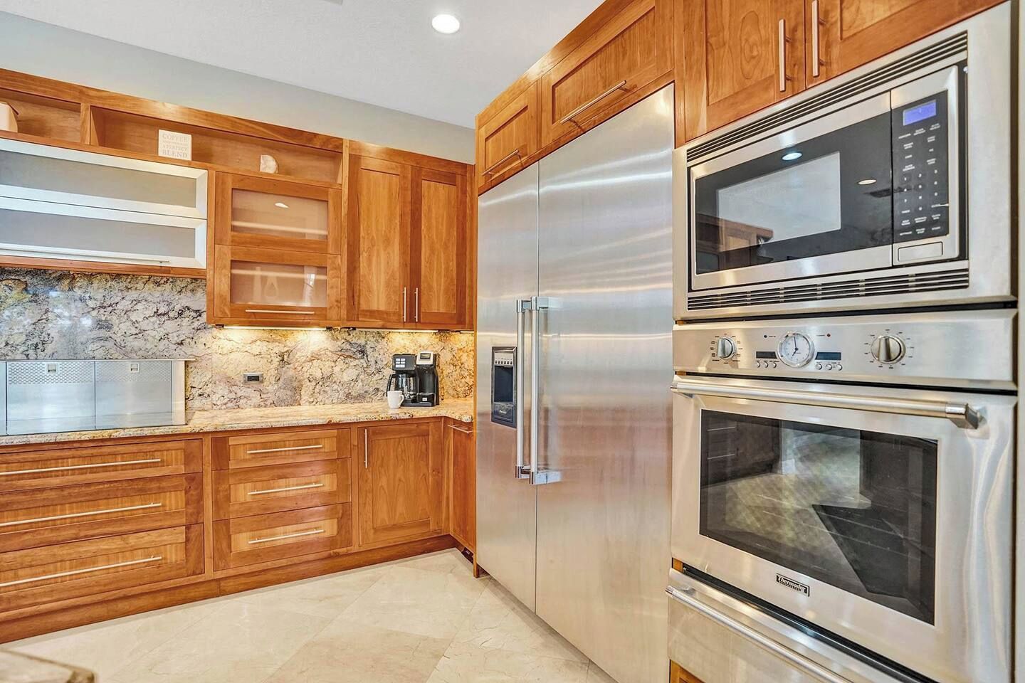 A modern kitchen with stainless steel appliances, wooden cabinets, and a marble countertop.