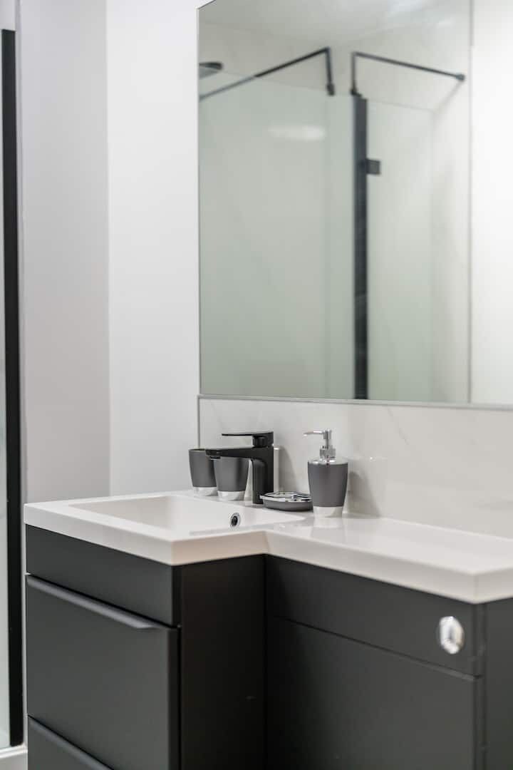 Une salle de bain moderne avec un lavabo blanc, des meubles noirs et un grand miroir.