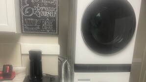 Un cuarto de lavado con lavadora y secadora LG de carga frontal, un mueble pequeño con cajones y una cafetera en la encimera.