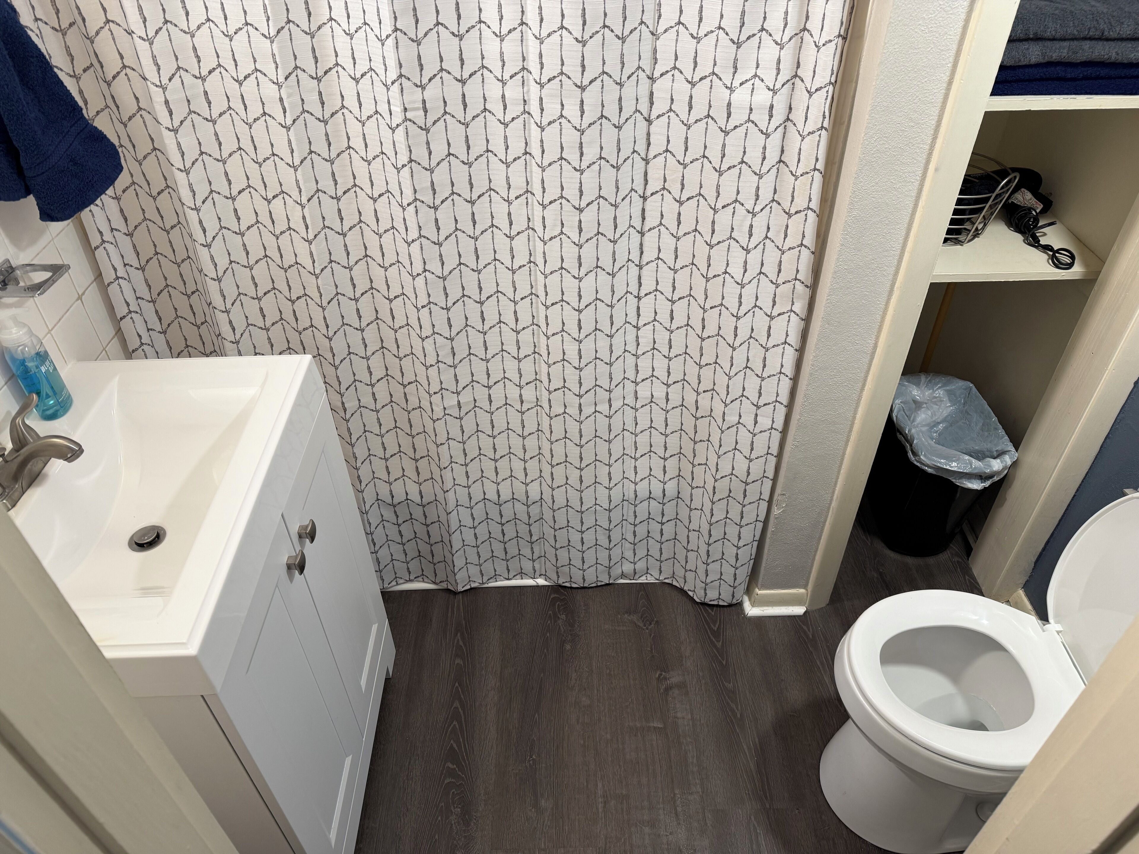 A bathroom with a patterned shower curtain, a sink with a faucet, a toilet, and a trash bin.