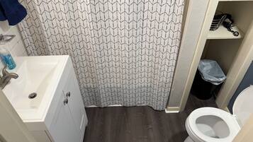 A bathroom with a patterned shower curtain, a sink with a faucet, a toilet, and a trash bin.