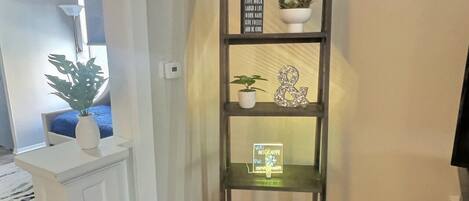 A corner bookshelf with multiple shelves, each holding decorative items and small plants.