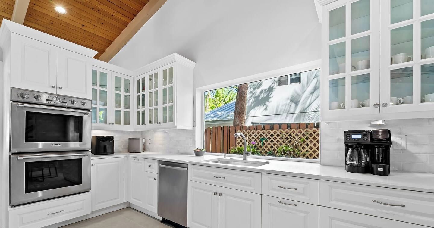 A modern kitchen with white cabinets, a built-in oven, a dishwasher, and a coffee maker.