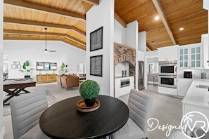 A modern living space with a wooden ceiling, a fireplace, a kitchen with stainless steel appliances, and a round dining table with a potted plant. - Villa w/Pool, Firepit & BBQ (Dania Beach)