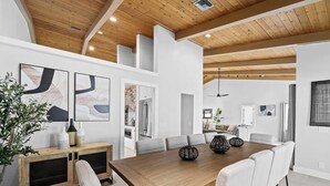 A spacious dining area with a wooden table and white chairs, a kitchen visible through an open door, and a ceiling fan. - Villa w/Pool, Firepit & BBQ (Dania Beach)