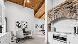 A modern kitchen with a brick fireplace, white cabinetry, and a dining area with a table and chairs. - Villa w/Pool, Firepit & BBQ (Dania Beach)