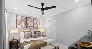 Ein Hotelzimmer mit einem Bett, zwei Nachttischen, einem Deckenventilator und abstrakter Wandkunst.