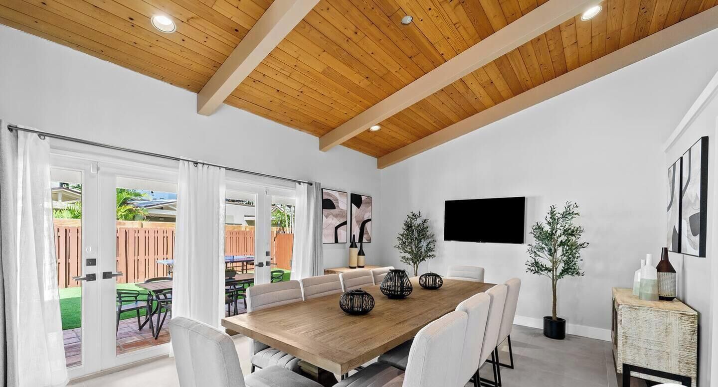 A dining area with a wooden table, white chairs, and a TV mounted on the wall.