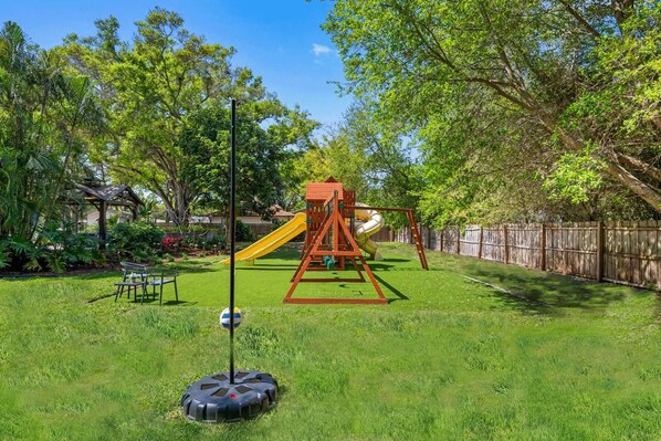 A backyard with a swing set, a slide, a bench, and a lawn. - Pool - Basketball -Soccer - Game Room - Playground (Largo)