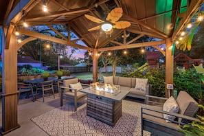 Un patio al aire libre con fogata, asientos e iluminación colgante.