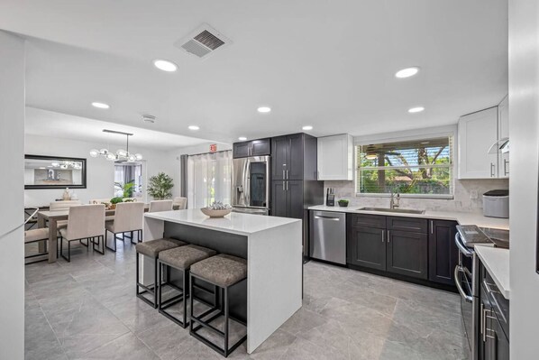 A modern kitchen with a central island, dark cabinetry, and a dining area with bar stools. - Pool - Basketball -Soccer - Game Room - Playground (Largo)