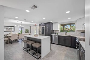 A modern kitchen with a central island, dark cabinetry, and a dining area with bar stools. - Pool - Basketball -Soccer - Game Room - Playground (Largo)