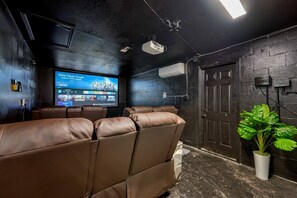 Un'area dedicata al cinema domestico con poltrone in pelle reclinabili, un ampio televisore a schermo piatto che mostra l'interfaccia di un servizio di streaming e una pianta in vaso.