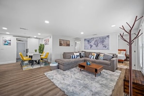 A modern living room with a grey sectional sofa, a wooden coffee table, and a grey shag rug. There is a dining area with a white table and yellow chairs. - Spacious 4BR w/ pool, BBQ grill & theatre room (Bradenton)