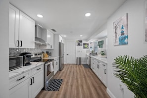 A modern kitchen with white cabinetry, stainless steel appliances, and a wooden floor. - Spacious 4BR w/ pool, BBQ grill & theatre room (Bradenton)