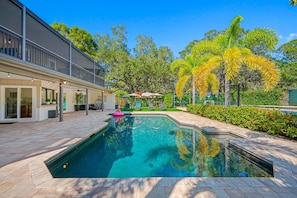 A swimming pool with a pink flamingo float, surrounded by a patio area with outdoor furniture and a covered seating area.