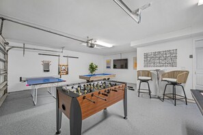 A room with a foosball table, ping pong table, and a pool table. There are two chairs and a TV mounted on the wall. - Pool - Pickleball - Basket - Soccer - Game Room! (Seminole)