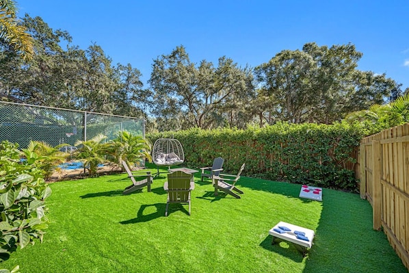 A backyard with a lawn, a swing chair, a lounge chair, and a small table.