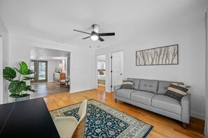 A spacious living room with a grey sofa, a ceiling fan, and a large plant.