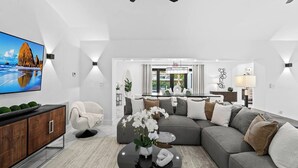 Un salon moderne avec un canapé d’angle, un téléviseur à écran plat, une table basse ronde ornée d’un vase de fleurs et un ventilateur de plafond.