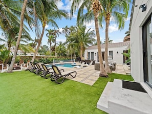 A pool area with lounge chairs, palm trees, and a clear sky. - Spacious home w/ heated pool & jacuzzi (Hollywood)
