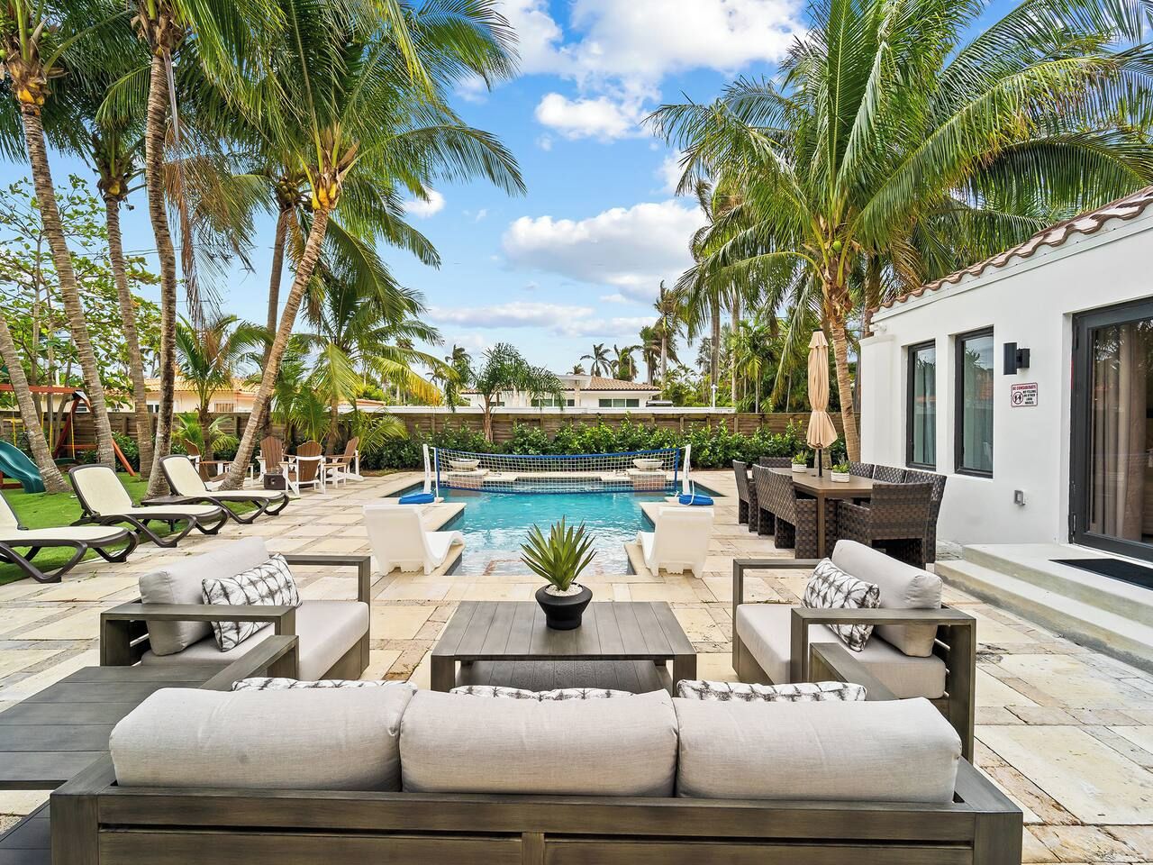 A poolside area with lounge chairs, a pool, and palm trees.