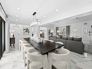 A modern living room with a dark wooden dining table, white chairs, and a grey sofa. - Spacious home w/ heated pool & jacuzzi (Hollywood)