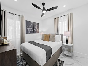 A modern hotel room with a bed, a bedside table with a lamp, a ceiling fan, and artwork on the wall. - Spacious home w/ heated pool & jacuzzi (Hollywood)