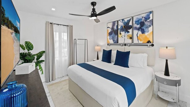 Une chambre d’hôtel moderne dotée d’un grand lit, d’un ventilateur de plafond, d’œuvres d’art au mur et offrant une vue sur la plage.