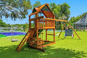 A wooden playhouse with a ladder, a slide, and a swing set in a park. - Pool - Pickleball - Soccer - Basket - Sleeps 18! (Tampa)