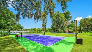 An outdoor tennis court with a net, surrounded by grass and trees. - Pool - Pickleball - Soccer - Basket - Sleeps 18! (Tampa)