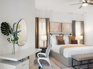 Habitación de hotel con cama, mesitas de noche, escritorio, silla, espejo y ventilador de techo.