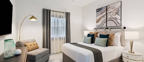 A modern hotel room with a large bed, a desk, a chair, a TV, and a ceiling fan.