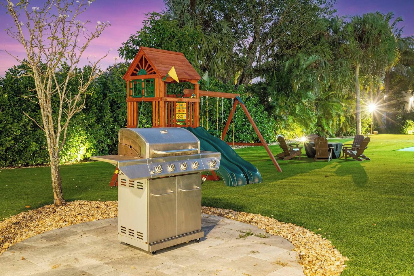 Patio trasero con una parrilla, un columpio y una casita de madera.