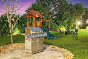 Patio trasero con una parrilla, un columpio y una casita de madera.