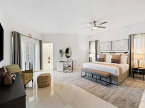 A modern hotel room with a large bed, a desk, a chair, and a ceiling fan.
