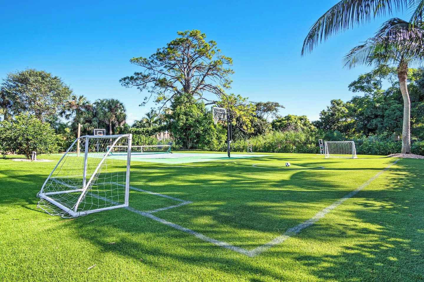 A well-maintained grassy field with two soccer goals, surrounded by trees and a clear sky.