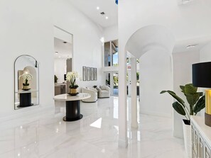 Een ruime, moderne lobby met een gepolijste marmeren vloer, een ronde tafel met een bloevas en een zithoek met banken.