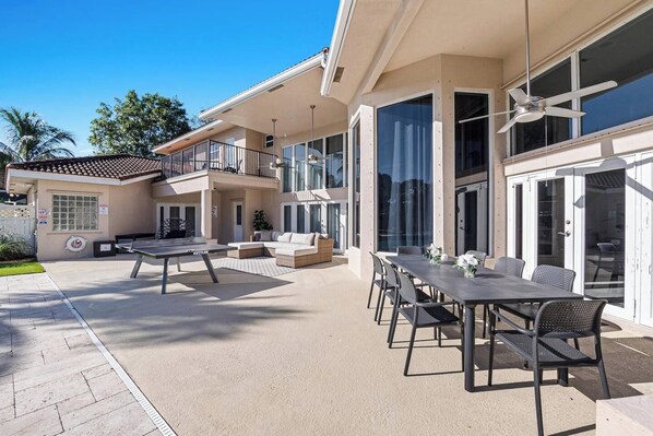 A modern outdoor patio with a pool table, seating area, and a covered dining space.